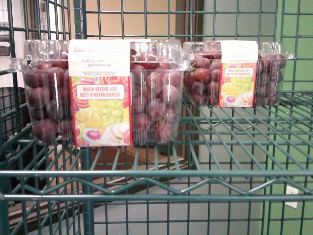 Three clamshell containers of red grapes on a shelf.